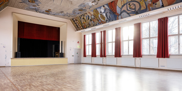 Evenemangslokal Albrektssalen: Allrum med scen,  höga fönster, röda gardiner och målning i taket.