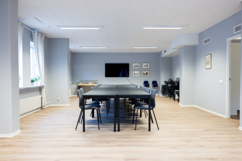 Kvarterslokal Fenix: Allrum med bord, stolar och TV på väggen.