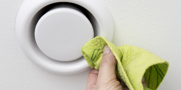 En person som rengör en ventilationsdon med en trasa