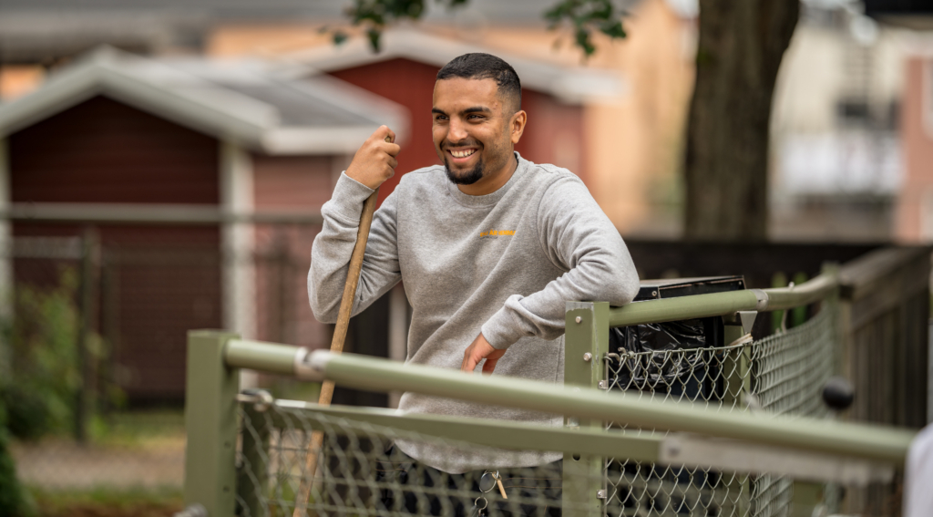 En ung kille står på en innergpård och håller i en kvast. 