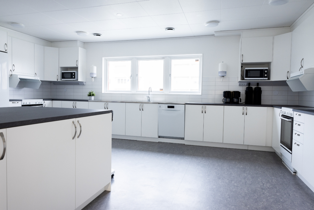 Kvarterslokal Nocken: kök med vita skåp och svarta bänkskivor. Diskmaskin, spis, ugn och micro.