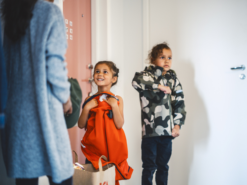 Två barn som står i en hall och klär på sig ytterkläder.