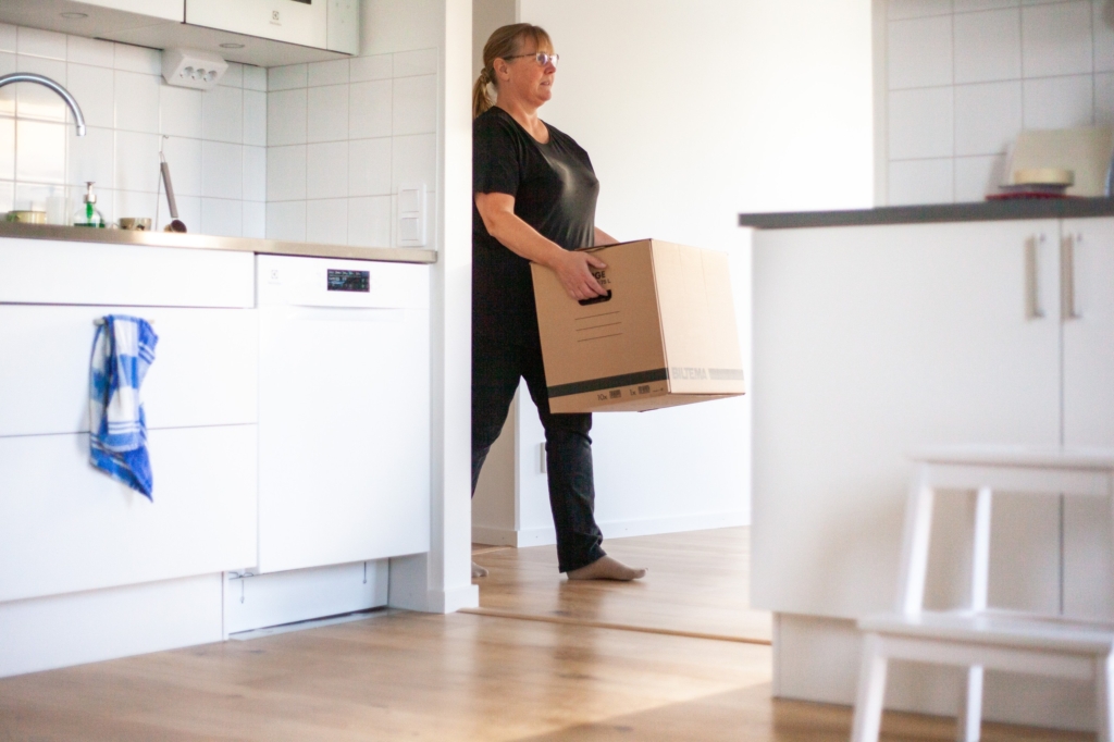En kvinna går in i en lägenhet och bär på en flyttkartong.