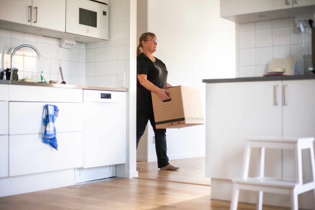 En kvinna går in i en lägenhet och bär på en flyttkartong.