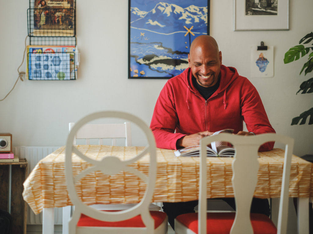 En man sitter vid ett köksbord och läser en bok. 