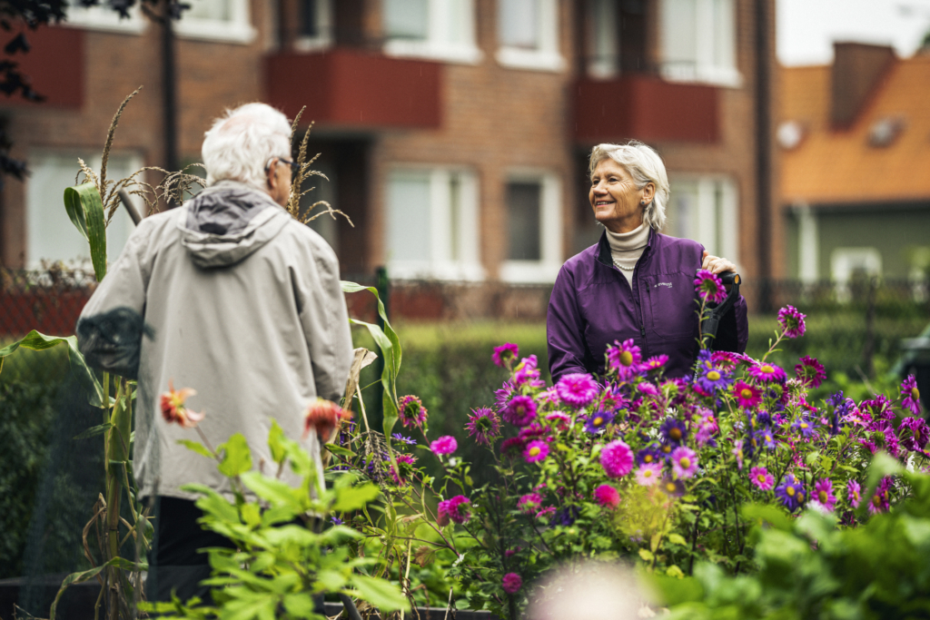 Två seniorer som pratar med varandra i en trädgård.