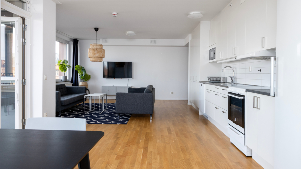 Interiörbild av en Bo tillsammans-lägenhet i Kopparhusen. Öppen planlösning med kök och vardagsrum med köksbord och soffgrupp.