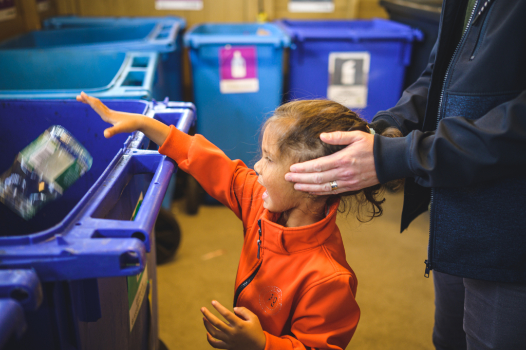 Ett litet barn som källsorterar i ett miljörum.