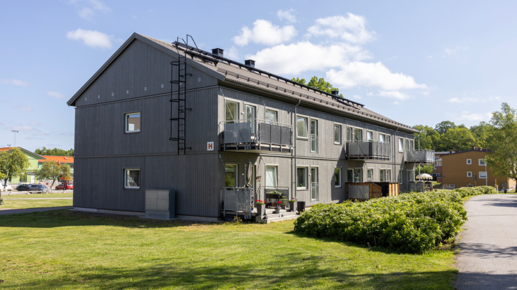 Grått tvåvåningshus med tre balkonger på ovanvåning samt tre uteplatser på markplan.