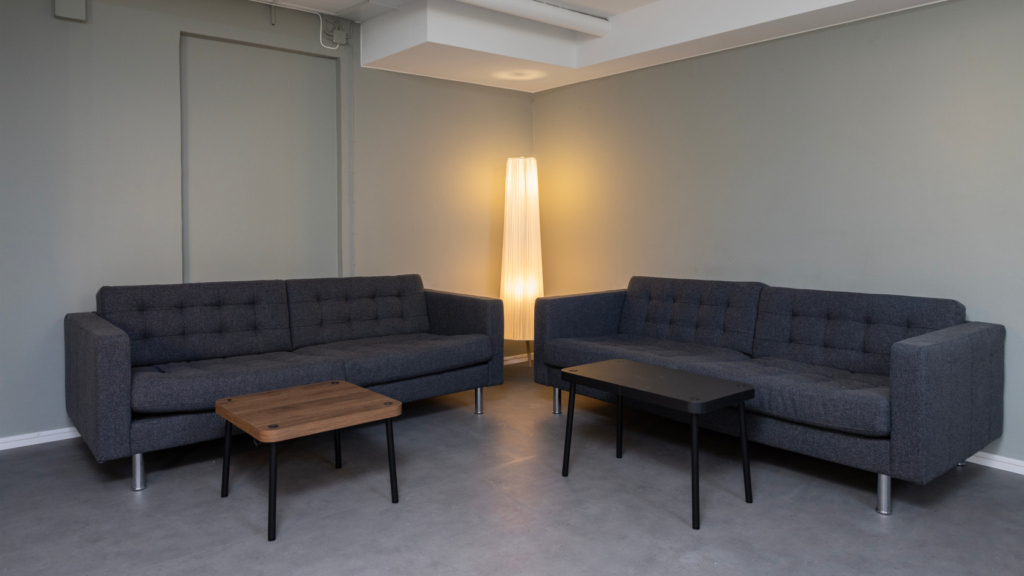 Allrum på Assesorn med ljusgröna väggar. Två mörkgrå soffor som står vända mot varandra och framför finns två soffbord.