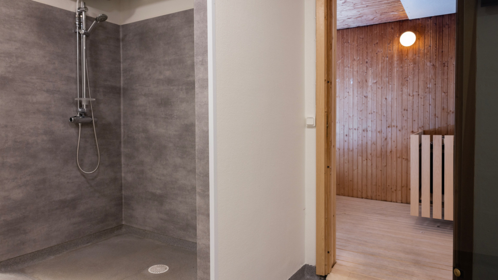 Bastu på Assessorn. Till vänster i bild syns ett duschrum med mörkgråa väggar. Till höger syns bastun och ett aggregat.