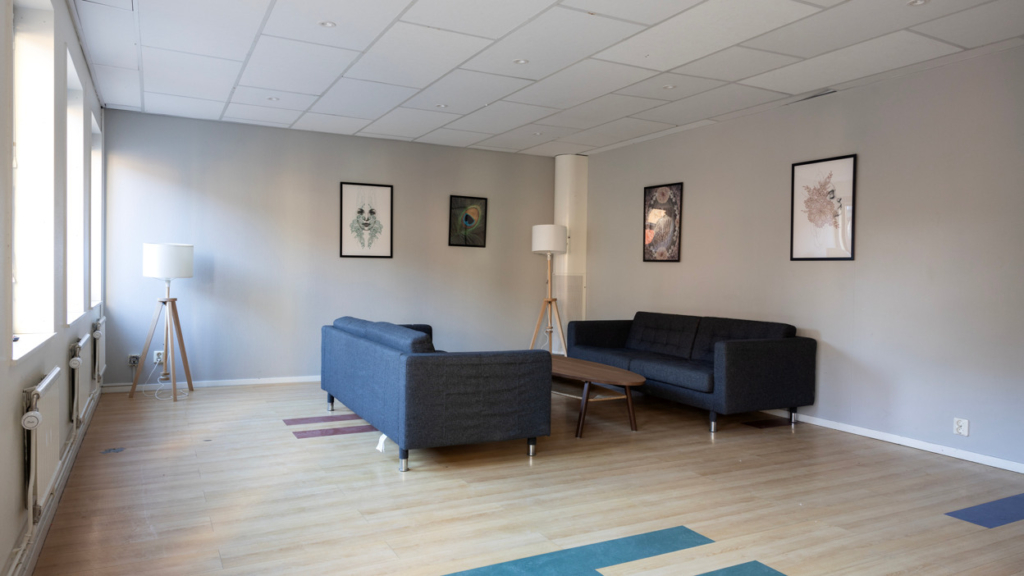 Ett allrum på Bryggeriet med ljus trägolv och ljusgrå väggar. I rummet finns två soffor med ett litet soffbord i mitten.