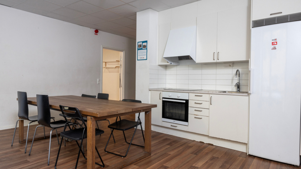 Dalkarlens allrum med kök. Spis, kyl samt bord och stolar finns.