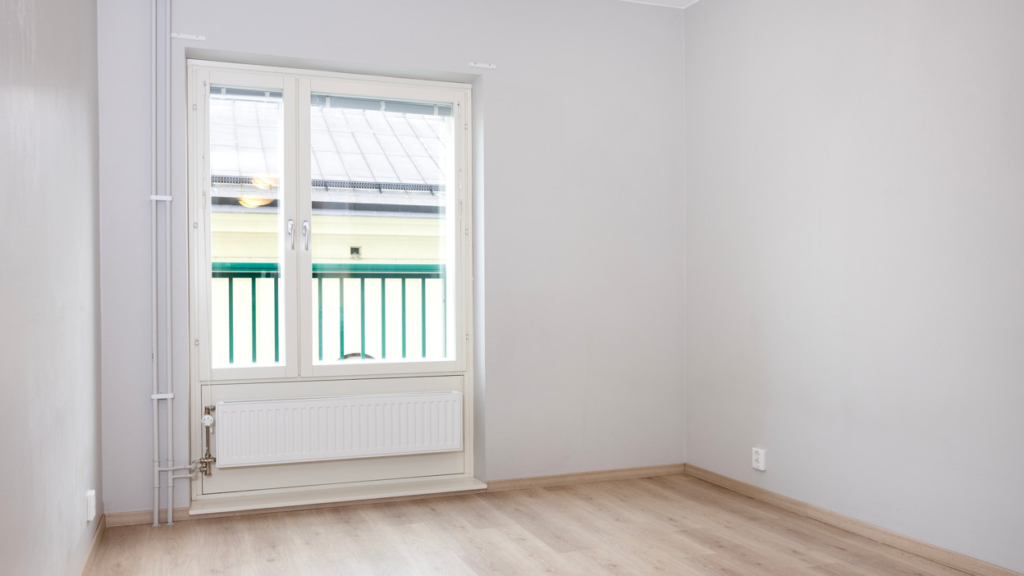 Insidan på en av lägenheterna på studenthuset Klockan. Väggarna är vita och golvet är ljust trä. Genom fönstret ser man en grön fasad.