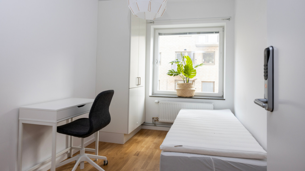 Ett av rummen i våra coliving-lägenheter. I rummet finns en säng, skrivbord med stol och en garderob.