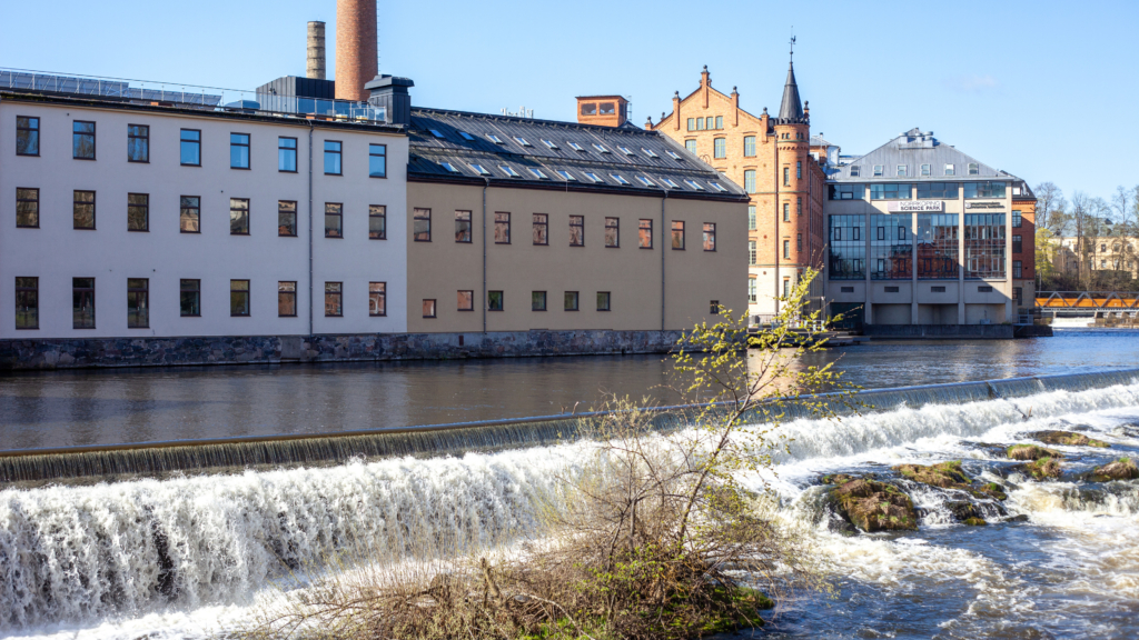 Linköpings universitet, Campus Norrköping, byggnad Kopparhammaren. I förgrunden syns Motala ström som forsar i ett kort vattenfall.