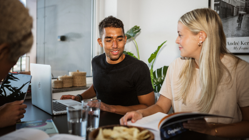 En grupp människor som sitter vid ett bord med en bärbar dator och studerar.