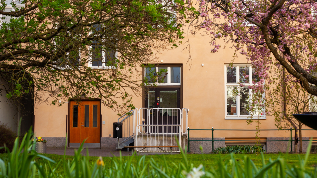 Entré från innergården till studentboende Täppan. Entrén är omgivet av träd och i förgrunden syns rabatt med tulpaner.