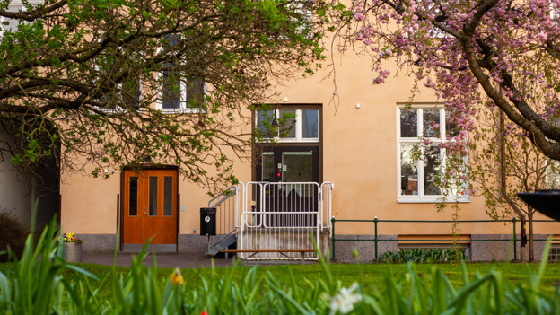 Entré från innergården till studentboende Täppan. Entrén är omgivet av träd och i förgrunden syns rabatt med tulpaner.