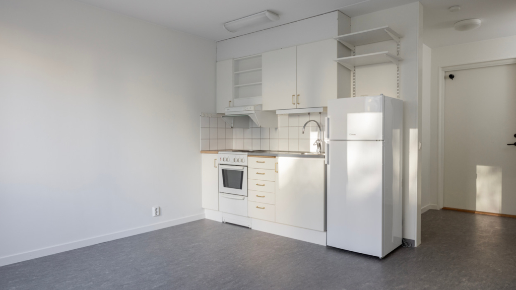 Interiörbild av en lägenhet på Konstantinopel. Bilden visar en köksdel med skåp, lådor, spis, kyl och frys och en hylla ovanför kylen. Till höger syns hallen och ytterdörren.